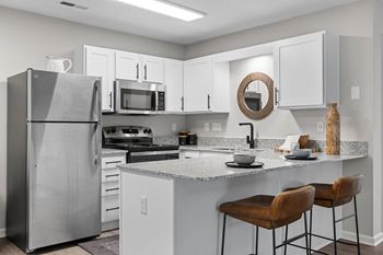 A kitchen with a refrigerator, microwave, oven, and bar stools.